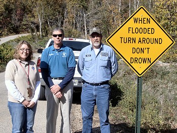 Baxter County Emergency Manager Jim Sierzchula (center) and Russel Duggins (right) of the Baxter County Road and Bridge Department stand next to a Turn Around Don't Drown sign along County Road 806 on 10/28/2011.