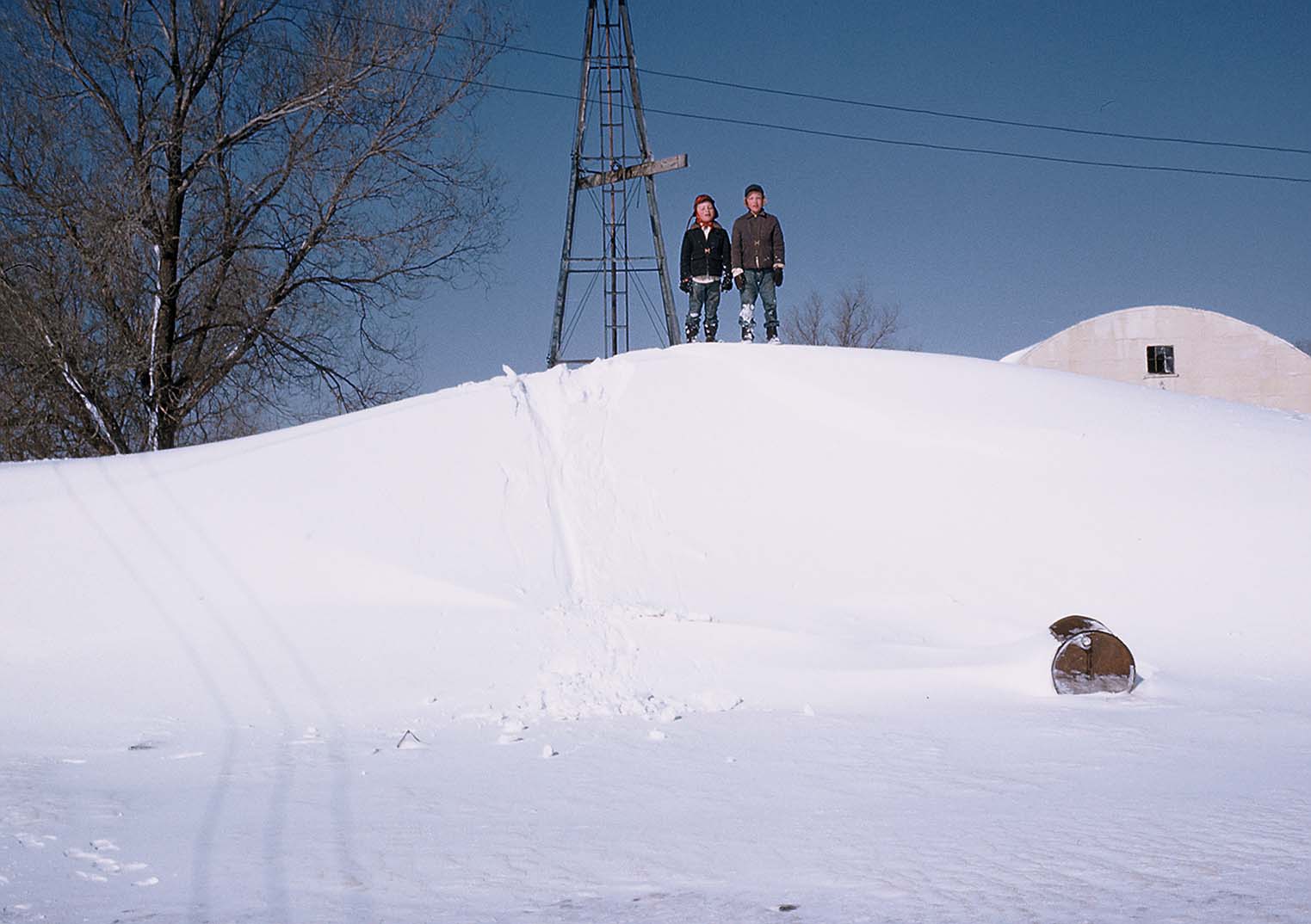 Kids standing on a snow drift that is covering the well house.