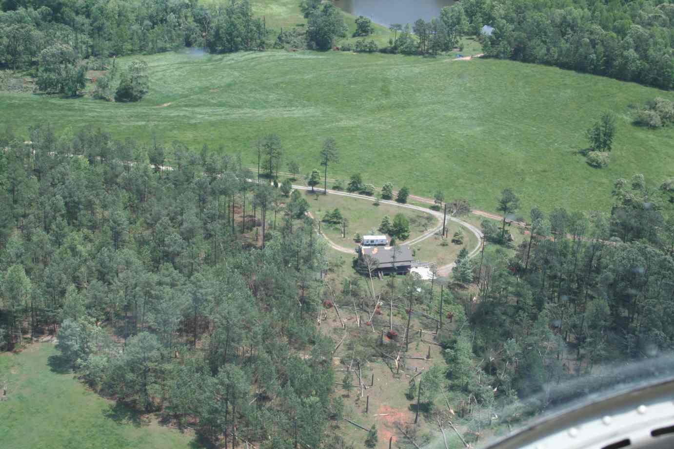 [ Aerial view of damage to home and tornado's path through wooded area. ]