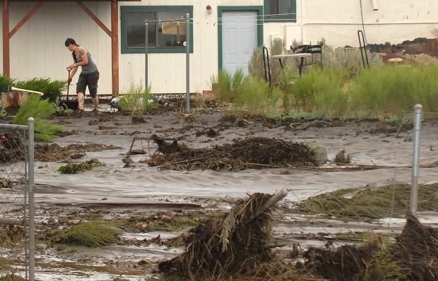 A resident is trying to keep debris away from their home as flood waters rush through their backyard.