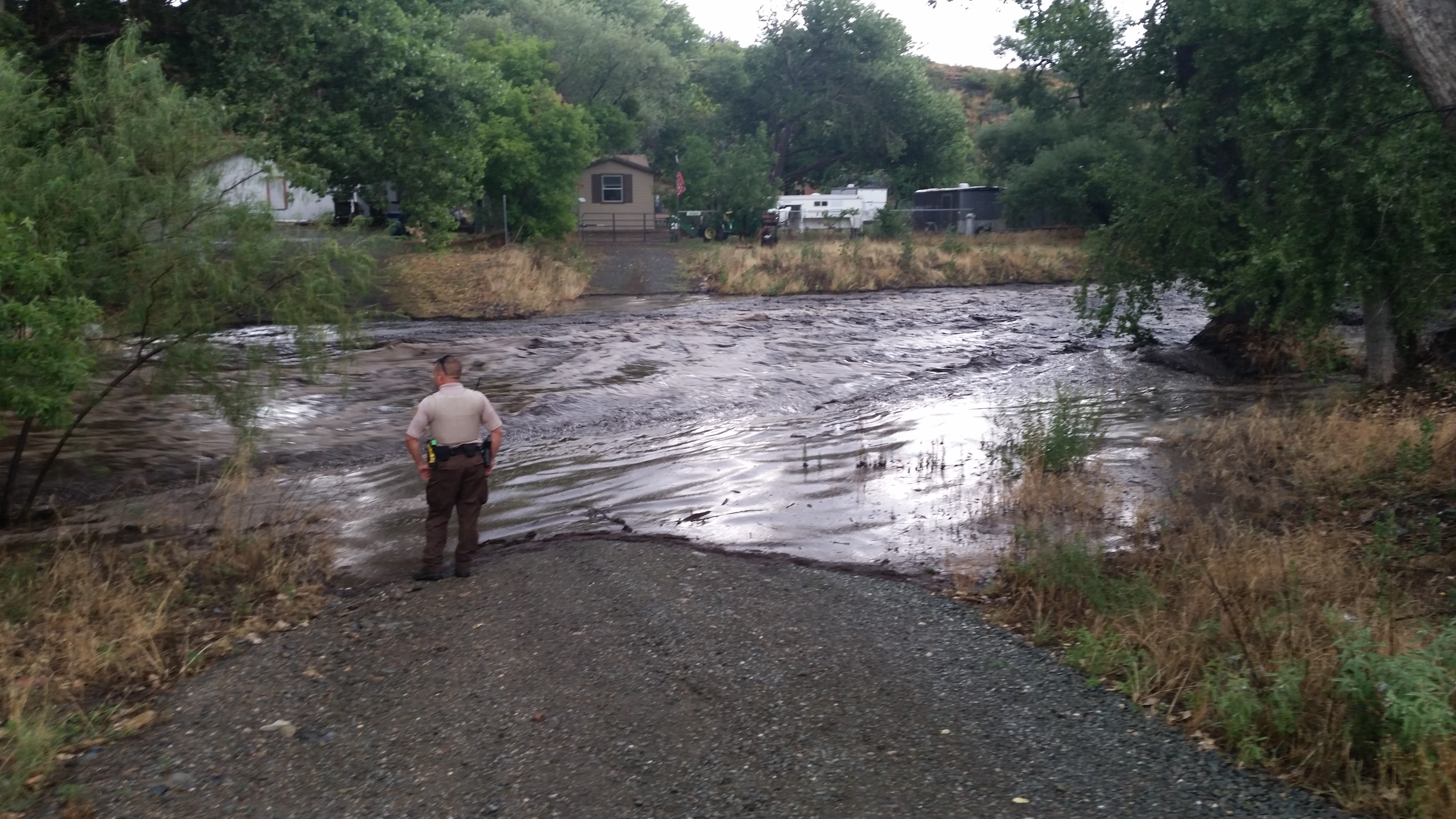 Law enforcement officer looks on at the flooding taking place along Central Avenue in Mayer, AZ as Big Bug Creek was overflowing the creek banks.