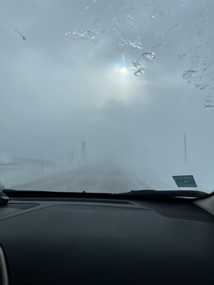 View from a vehicle front windshield of very low road visibility due to drifting snow.