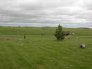 Debris scattered across yard and metal trusses down in the field. Notice the vacuum cleaner standing directly upright. Photo by NWS Staff.