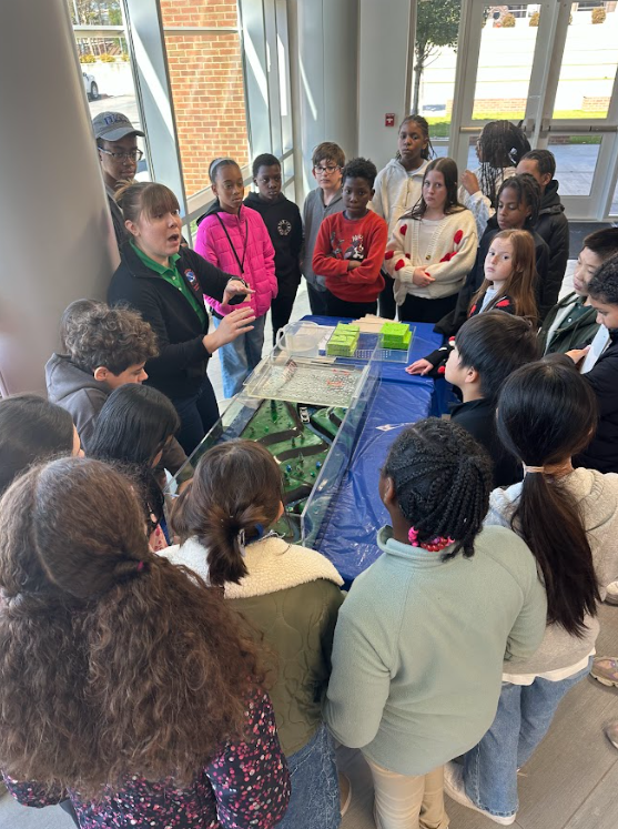 Children crowded around a hydrology model learning about flash flooding, river flooding, and flooding safety. 