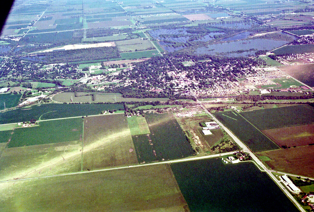 Photo showing damage path of 1990 Plainfield tornado from an airplane. Damage to buildings and vegetation is evident, which creates a clear path from near the foreground to the background. Photo vantage is from just west of Plainfield looking eastward