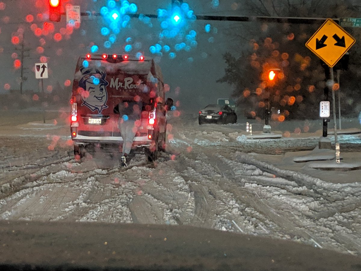 Photo of person pushing a stuck van to the side of the road at the intersection of Lindbergh and Schutz Road.