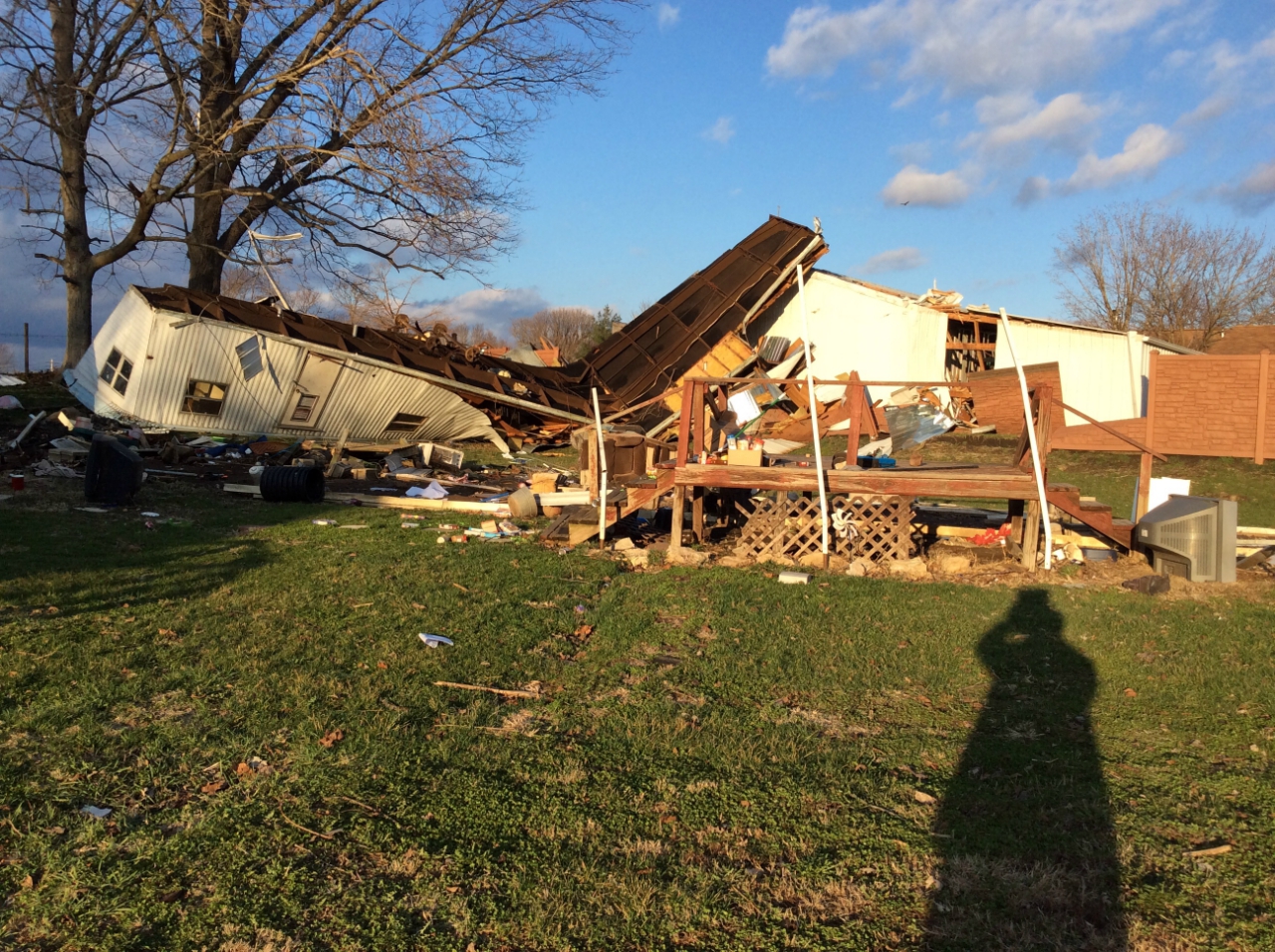 Photo of two empty mobile home trailers that were rolled. One just on its side and the other (pictured) on its top, with the end coming in contact with neighbors outbuilding crushing the end of the trailer and damaging the shed.