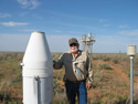 cooperative observer at the WIPP site in New Mexico standing beside a rain gauge
