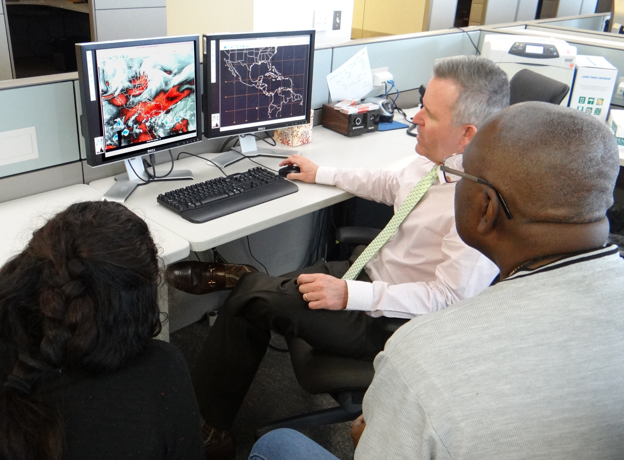 Fig. 1. Mike Davison (at the computer) is seen training Sareti Cardos from Mexico (left) and Earl Hunte from Barbados (right) on the analysis of water vapor imagery, to assess the upper tropospheric synoptic situation and the availability of moisture in the upper atmosphere.