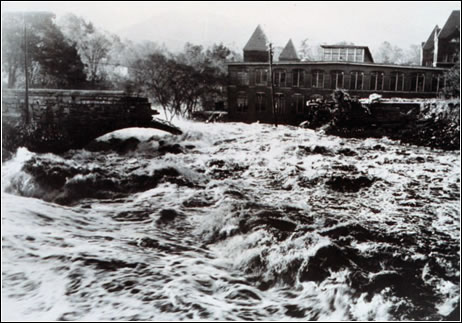 Rapid floodwaters from the Swift River in Ware, MA, destroy a stone bridge and flood buildings. (NOAA)