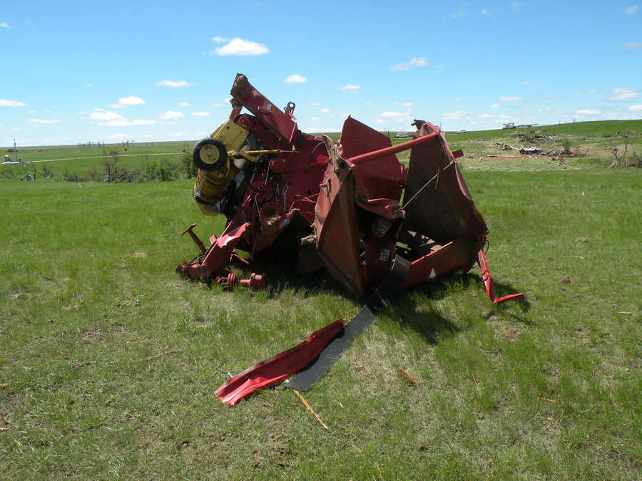 Destroyed round baler thrown about 300 yards from destroyed pole barn (distant, behind baler)