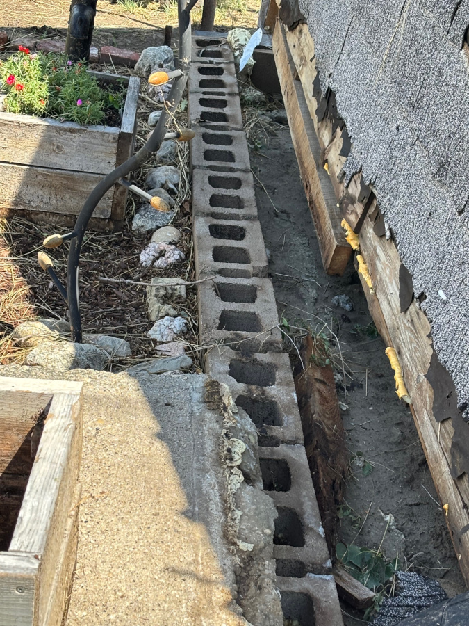  A cinder block retaining wall is shown next to the foundation of a building. The wall is partially covered in dirt and debris.