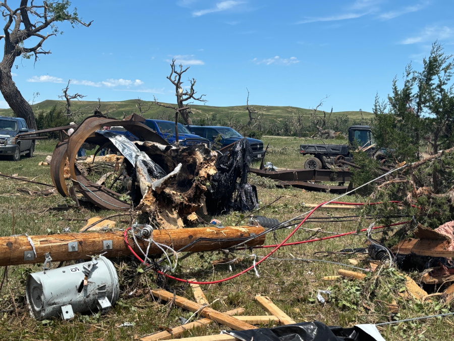 A broken utility pole and a transformer lie on the ground, surrounded by twisted metal and wood debris.