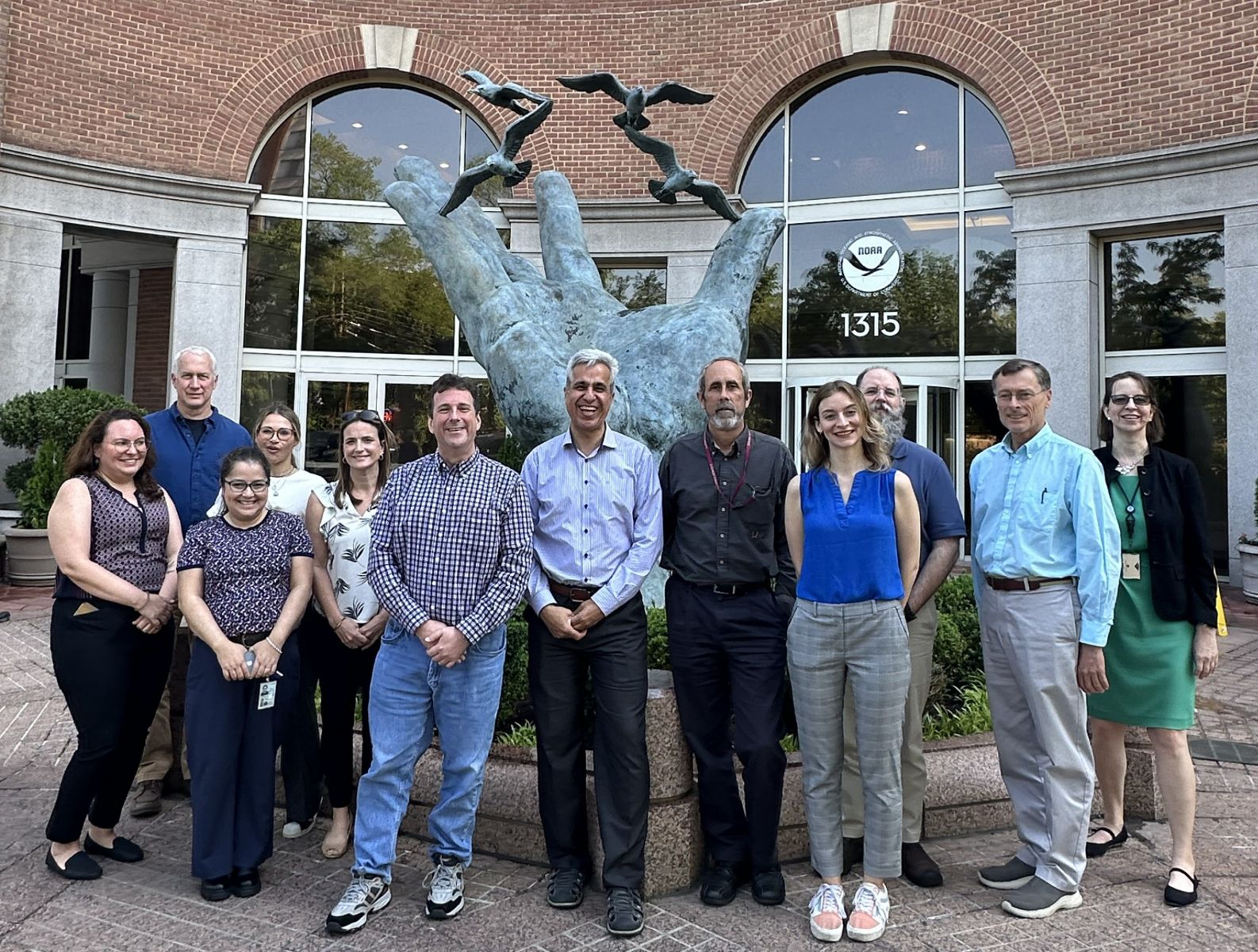 Image description: Coastal Coupling Community of Practice Super Friends (partial group) in front of a National Oceanic and Atmospheric Administration building and â€œThe Hand.â€ From left to right: Rebecca Atkins, John Warner, Cristina Urizar, Tracy Fanara, Courtney Barry, Trey Flowers, Saeed Moghimi, David Welch, Lucila Houttuijn Bloemendaal, Chris Massey, Rick Luettich, Dori Stiefel. Photo credit: A kind stranger.