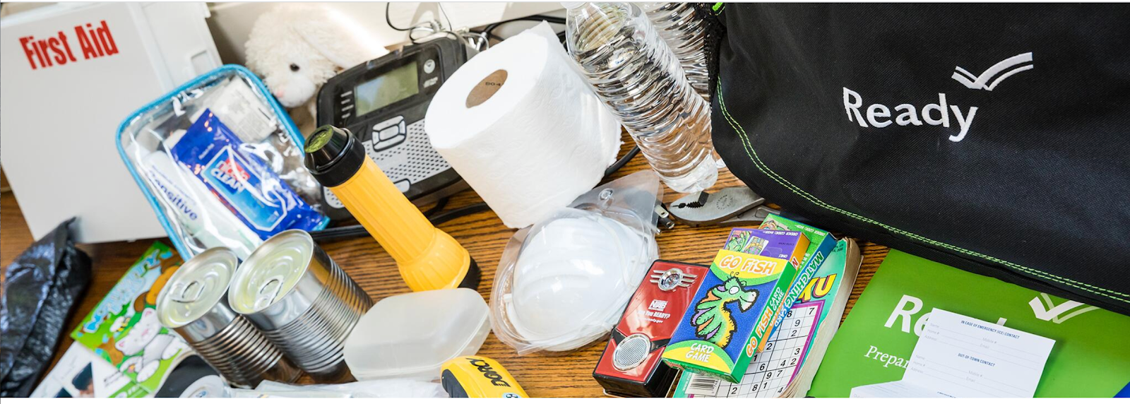Picture of emergency supplies including a first-aid kit, canned food, toilet paper, bottled water, flashlight, batteries, and other items.