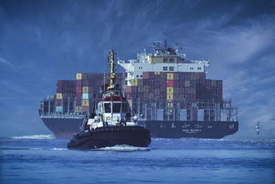 photograph of a small boat in front of a large container vessel in the ocean